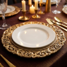 Load image into Gallery viewer, A close-up of a formal table setting featuring a white dinner plate centered on an ornate gold charger plate, with gold cutlery, candles, and a dark brown tablecloth in the background.
