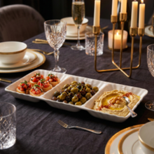 Lade das Bild in den Galerie-Viewer, A white rectangular three-compartment serving tray filled with appetizers, set on a dark tablecloth in a dining environment with candles, glasses, and plates.
